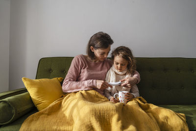 Mother checking temperature of sick daughter with thermometer at home