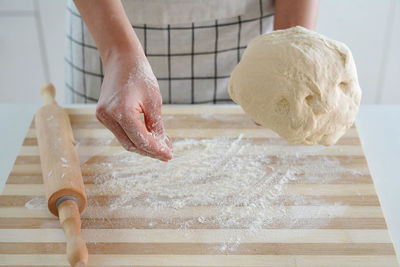 Woman puts flour on wooden table and holds dough in her hand. 