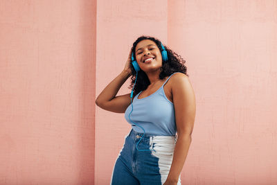 Young woman listening music against wall