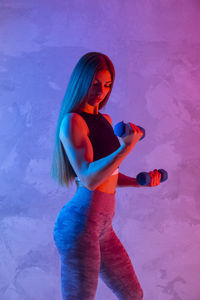 Woman lifting dumbbells standing against wall