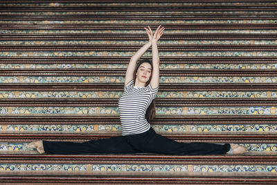 Ballet dancer with arms raised practicing splits on staircase