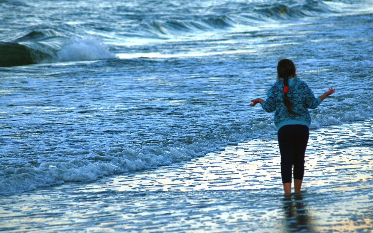 water, one person, leisure activity, lifestyles, real people, motion, sea, rear view, wave, women, beauty in nature, land, standing, beach, nature, adult, day, sport, outdoors, hairstyle, flowing water