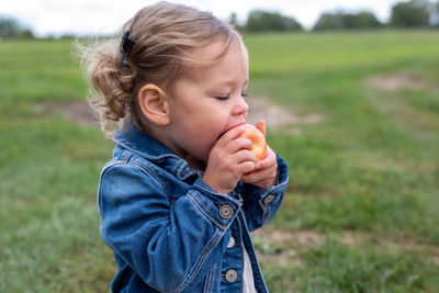 Cute girl eating apple standing on field