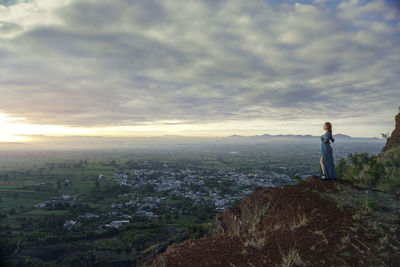 Rear view of woman standing on mountain against sky during sunset