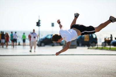 Young man doing stunt on road against sky in city