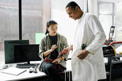 Female colleague discussing with male technician holding machine part at repair shop