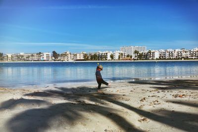 Side view of boy playing on shore at beach against city