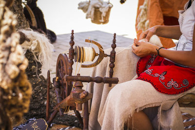 Midsection of woman sitting with loom on field