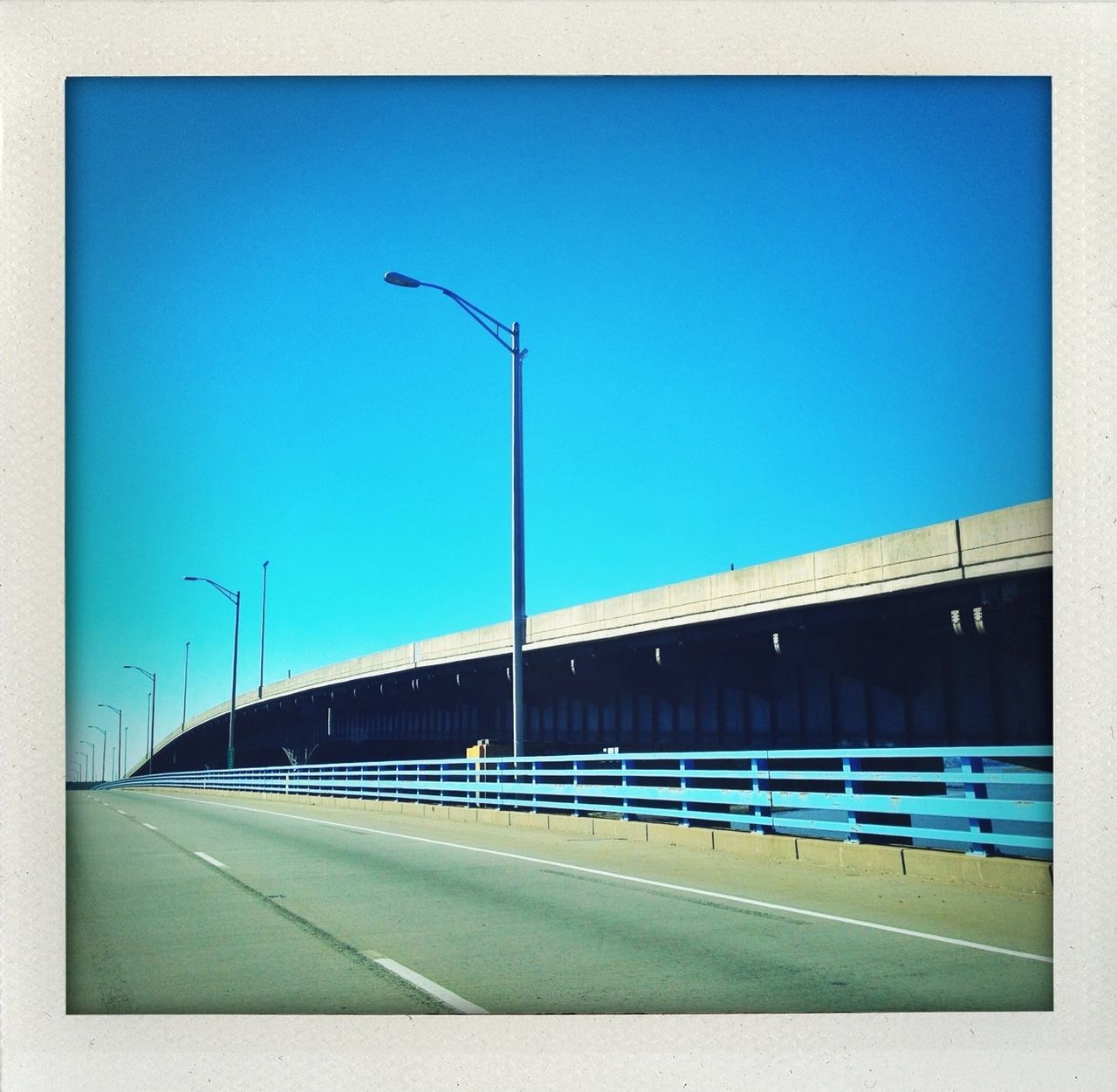 blue, road, clear sky, street light, transportation, road marking, built structure, the way forward, copy space, architecture, street, transfer print, building exterior, empty, asphalt, auto post production filter, sky, diminishing perspective, connection, outdoors