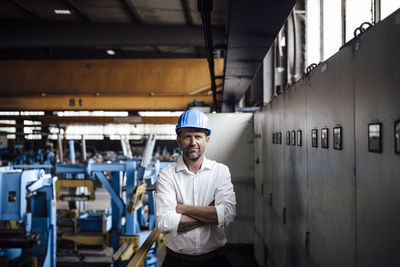 Smiling businessman with arms crossed standing in factory