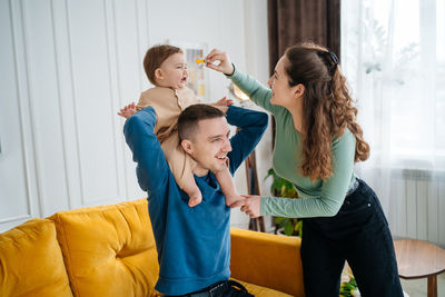 Baby on father's shoulders mom playing with little son gives the boy a pacifier