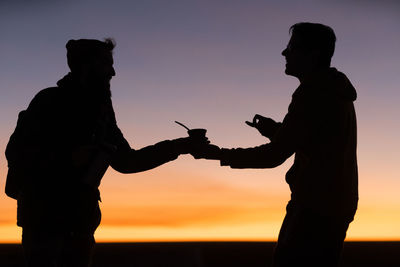 Silhouette man and friend standing against sky during sunset