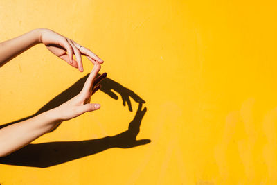 Cropped hands of woman gesturing against yellow wall