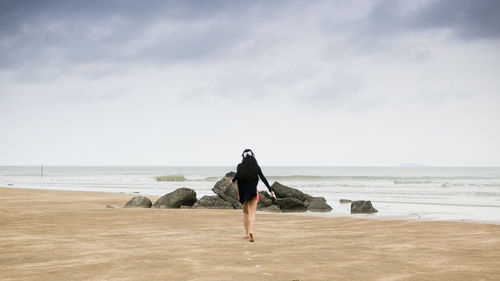 Rear view of woman on beach against sky