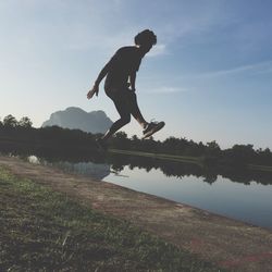 Side view of man jumping by lake against sky