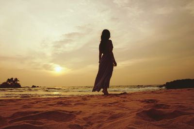 Woman walking at beach against sky during sunset