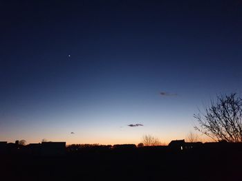 Silhouette trees on field against clear sky at sunset