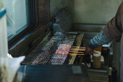 Midsection of person preparing meat on barbecue grill