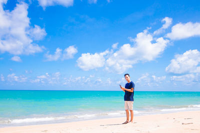 Portrait of man using mobile phone while standing on sand at beach