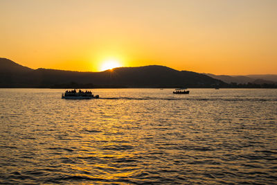 Silhouette boat sailing in lake against sky during sunset