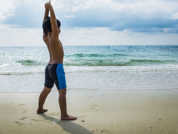 Full length of shirtless man standing on beach against sky