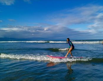 Teenage girl surfing on sea against sky