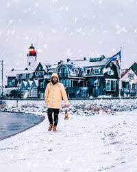 Full length of man walking on shore against buildings during snowfall