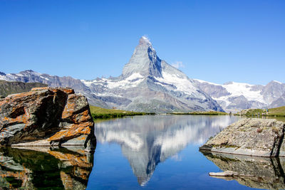 Scenic view of lake and mountains against clear blue sky