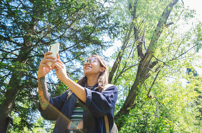 Woman smiles while using a smartphone in a lush green forest. sunlight filters through the trees.