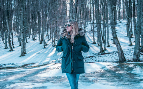 Portrait of smiling young woman standing in forest during winter