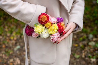 A woman's hand with a red manicure corrects a composition of autumn flowers in the pocket of a coat