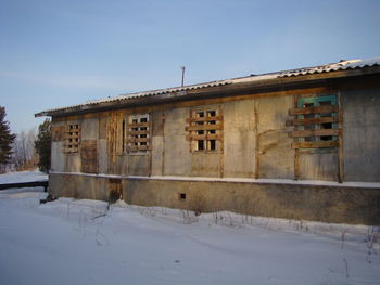 Abandoned building on snow covered field against sky
