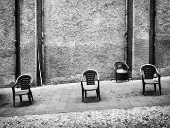 Empty chair on footpath against wall