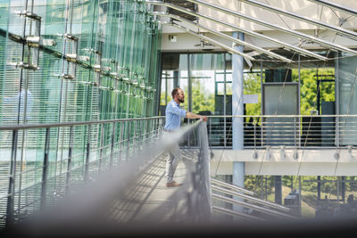 Thoughtful businessman standing at railing in modern office building