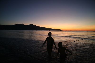 Silhouette people on beach against sky during sunset