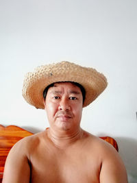 Portrait of shirtless man wearing straw hat sitting at home