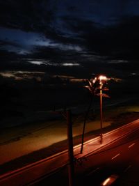 Illuminated street light on beach against sky at night