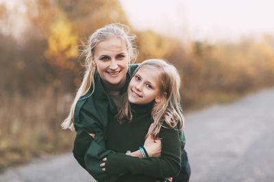 Happy mom and her blonde little daughter hugging and laughing while walking in autumn park