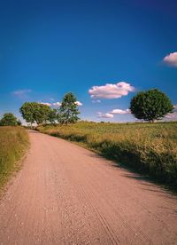 Road by trees on field against blue sky