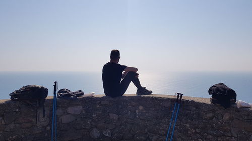 Low angle view of man walking on rock against clear sky and sea