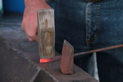 Midsection of man hammer metal in workshop