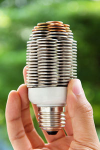 Close-up of hand holding light bulb with stack of coins