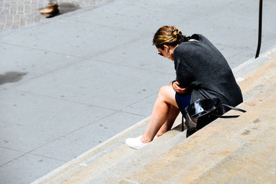 Side view of young woman sitting on steps during sunny day