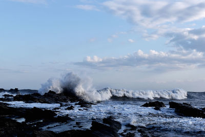 Waves splashing on rocks against sky