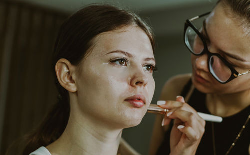 A young makeup artist applies blush to a girl s cheeks.