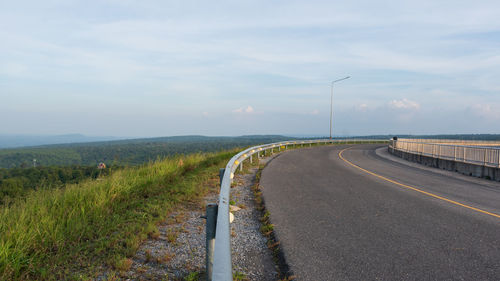 Empty road amidst field against sky