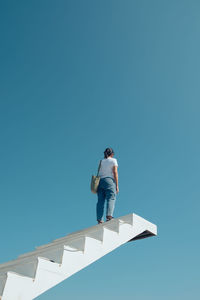 Low angle view of woman standing on steps against clear blue sky