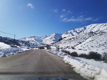 Snow covered road by mountains against sky