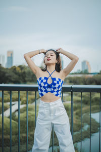 Portrait of young woman standing against railing