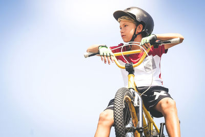 Low angle view of boy sitting on bicycle against clear sky